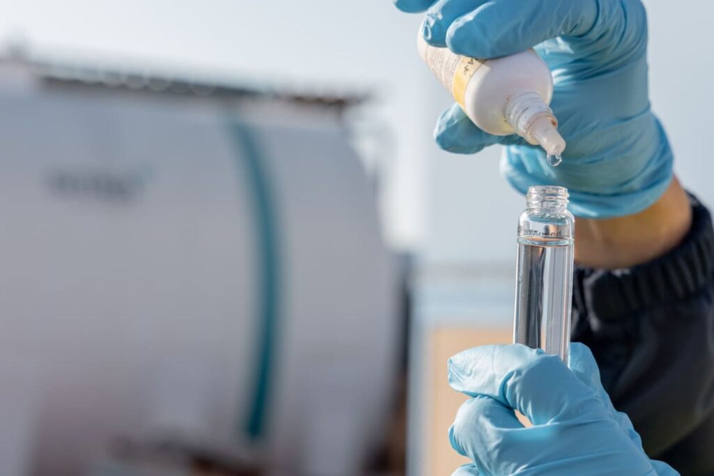 Persona con guantes poniendo un químico especializados para tratamiento de agua a un tubo de ensayo